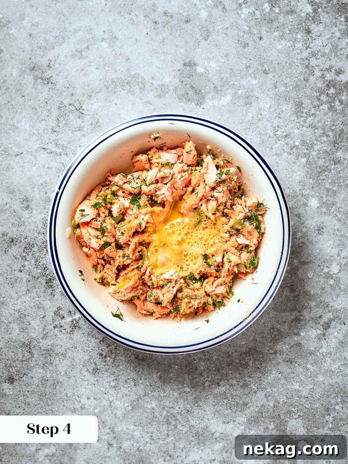 Egg being added to salmon patty mixture in a mixing bowl with herbs and breadcrumbs.