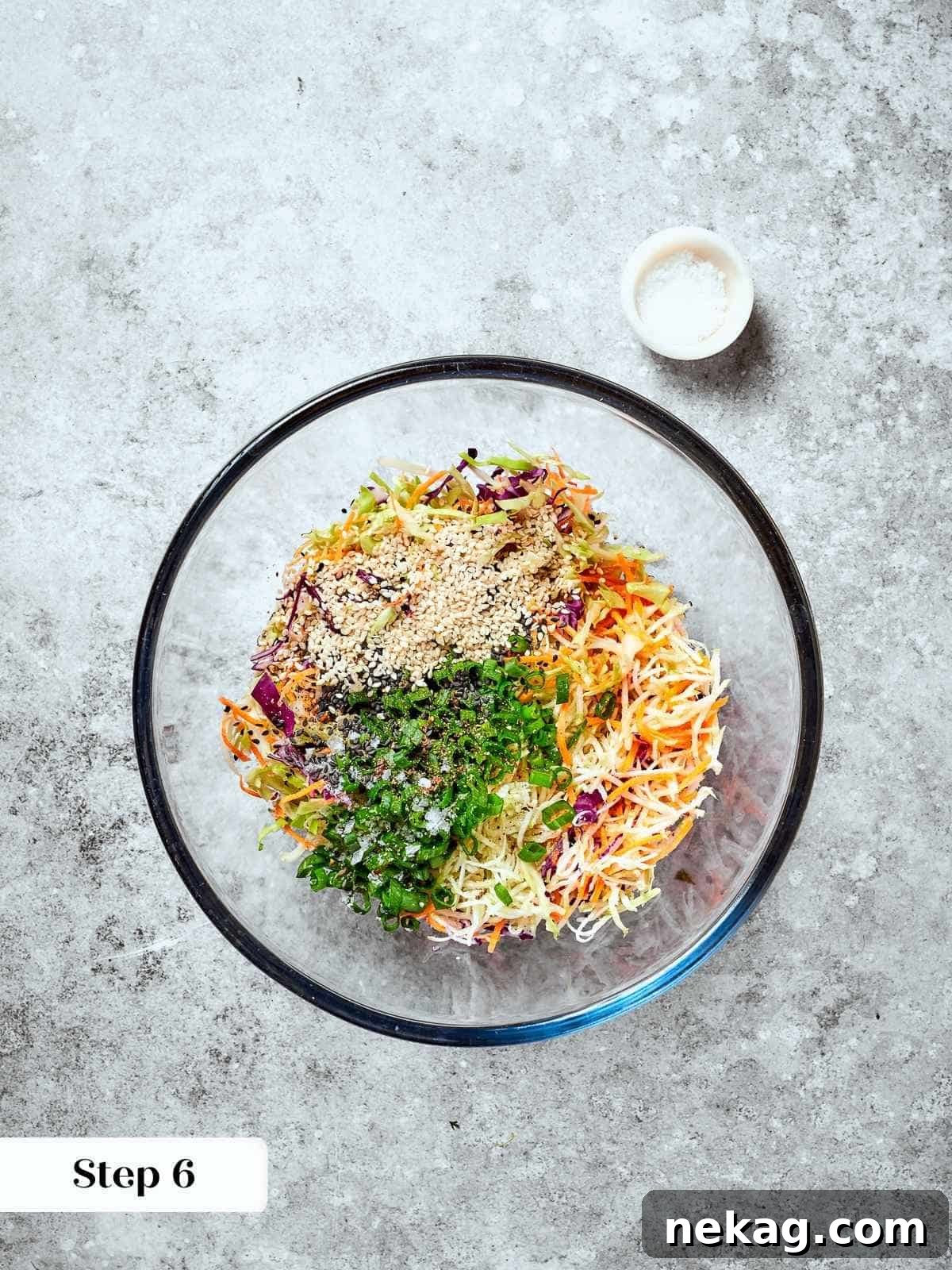 Mixing bowl filled with raw slaw ingredients, including broccoli mix and sesame seeds.