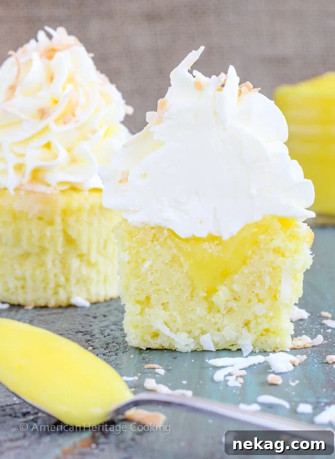 Lemon & Coconut Cloud Cupcakes 2 Beautifully decorated Lemon Coconut Cupcakes with a visible lemon curd filling and fluffy Italian Meringue Buttercream, garnished with toasted coconut.