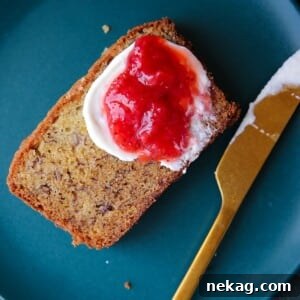 Moist banana bread slice shown with thick jam spread, resting on a small plate, ready to eat.