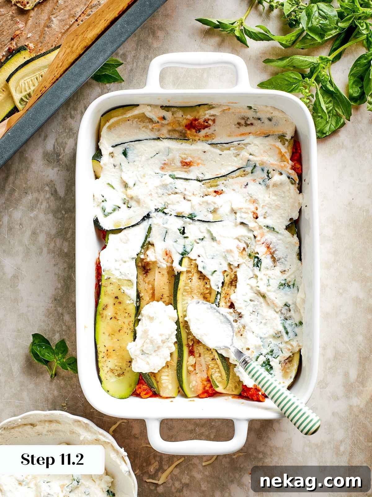 A smooth, even layer of herbed ricotta cheese is delicately spread over the roasted zucchini slices, adding a creamy and aromatic element to the lasagna assembly.