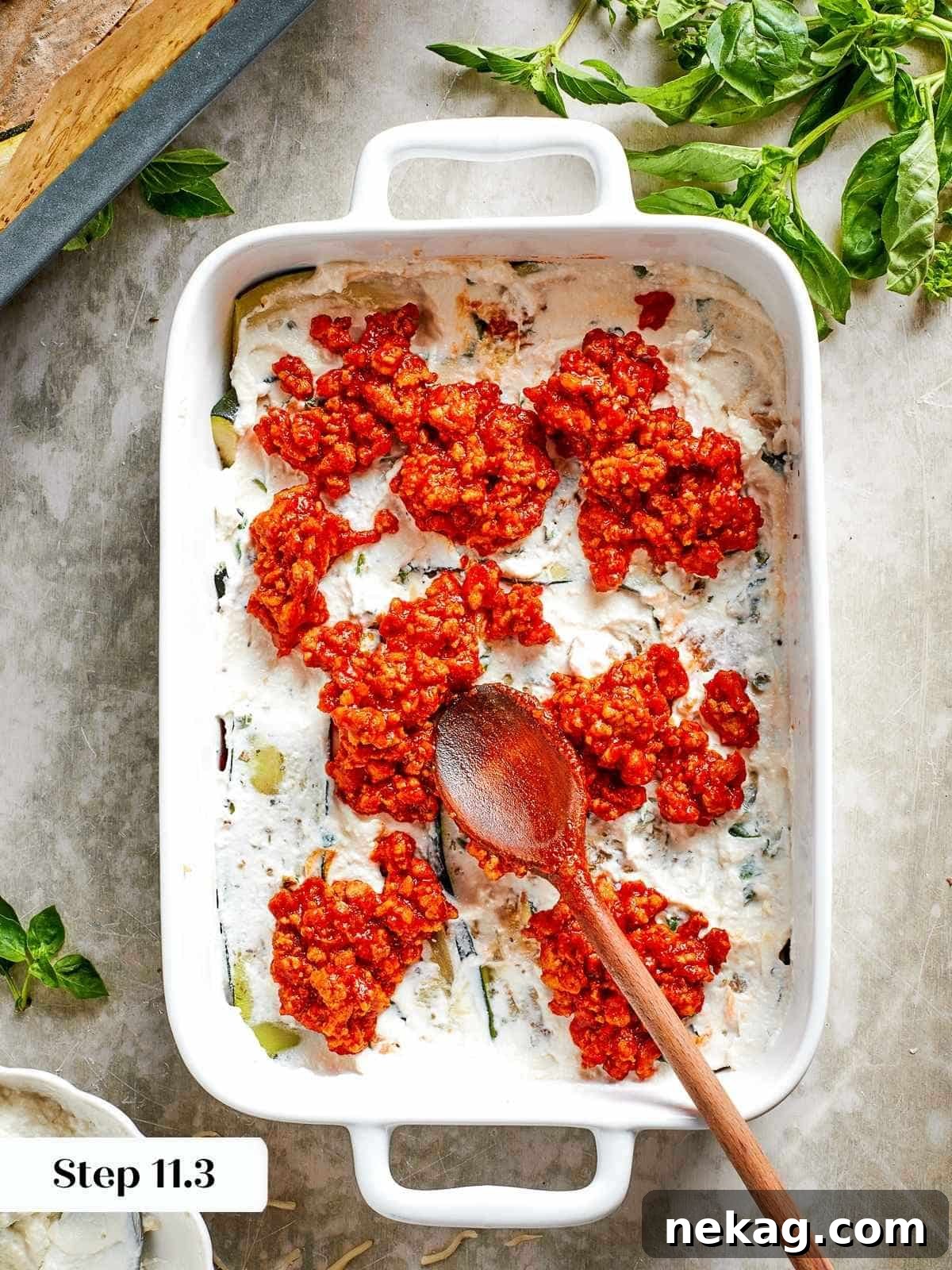A spoon meticulously spreading the rich tomato chicken sauce over a layer of creamy ricotta, demonstrating the careful layering in the zucchini lasagna.