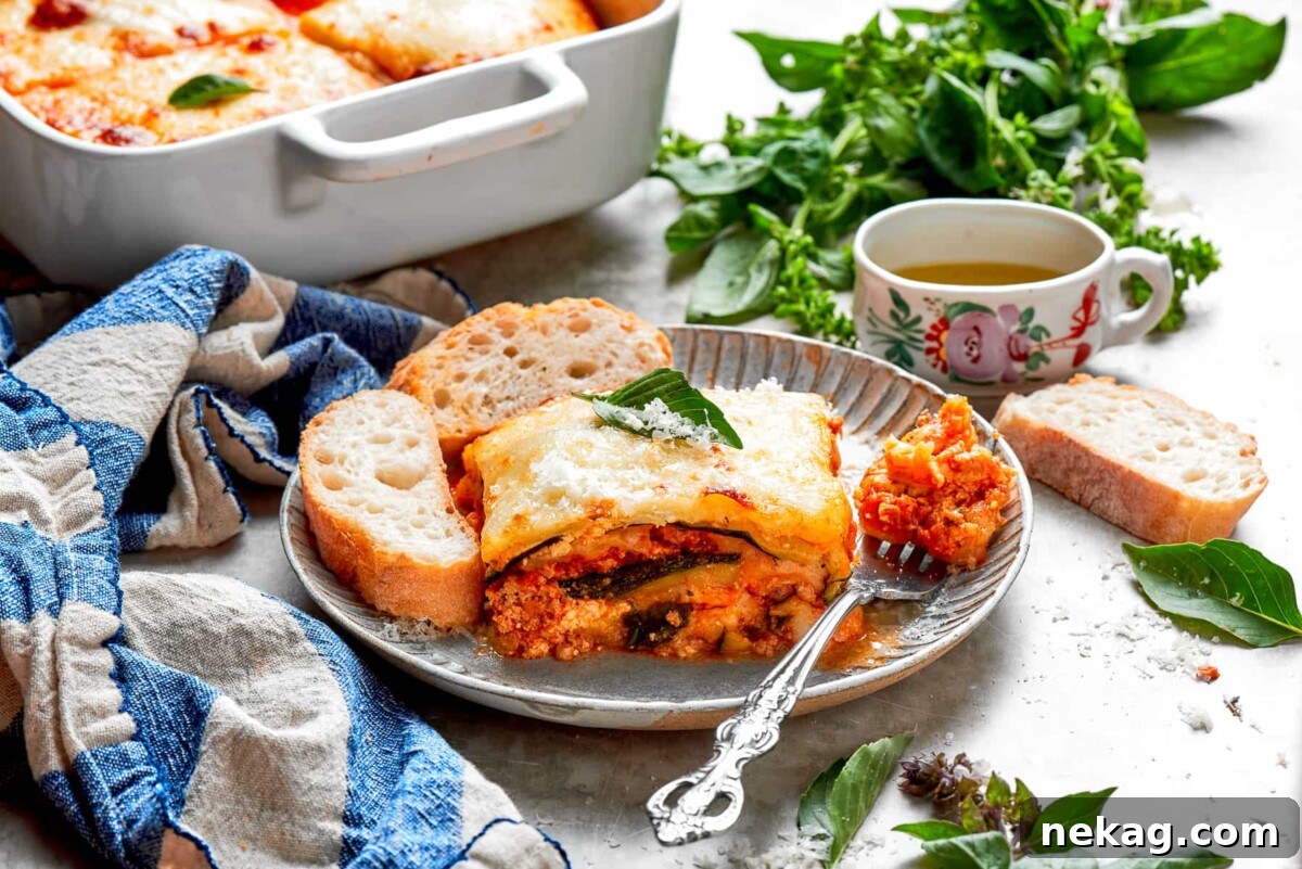 A perfectly portioned slice of Zucchini Lasagna, elegantly presented on a silver plate, revealing its neat, vibrant layers of zucchini, ricotta, chicken sauce, and melted cheese.