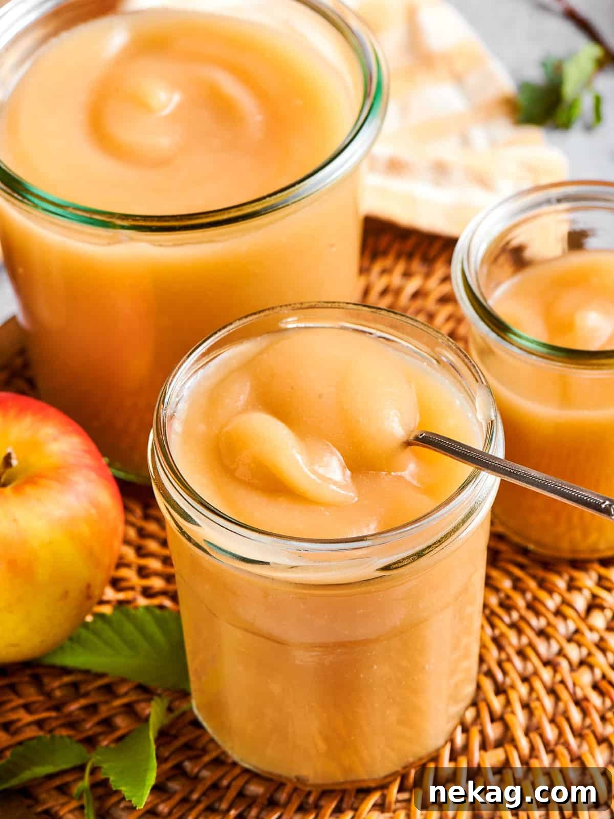 A spoon rests inside a jar of homemade applesauce, ready for serving at the table, highlighting its fresh appeal.
