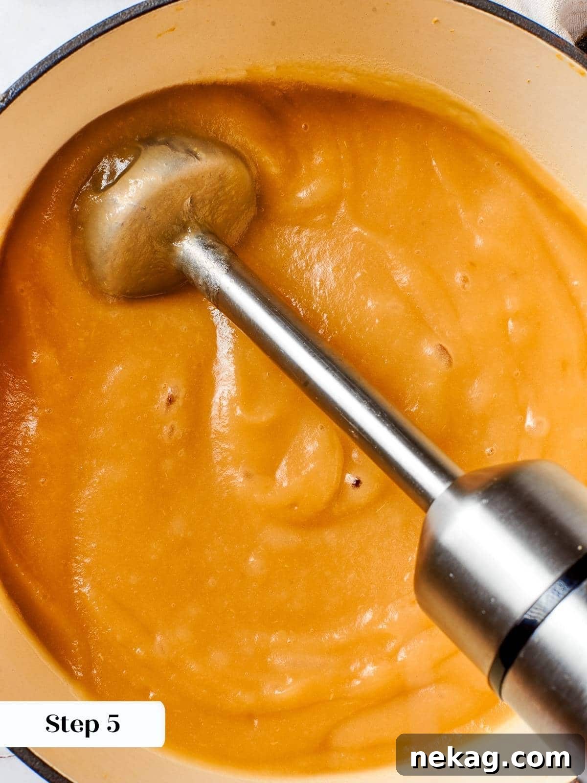 An immersion blender pureeing cooked apples directly in the pot to achieve smooth applesauce.