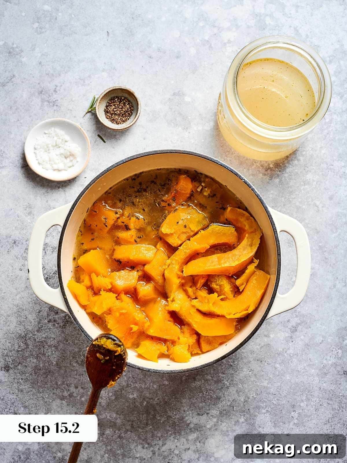 Rich vegetable stock being poured into a pot containing tender, cooked squash and aromatic vegetables, forming the liquid base for the creamy soup.