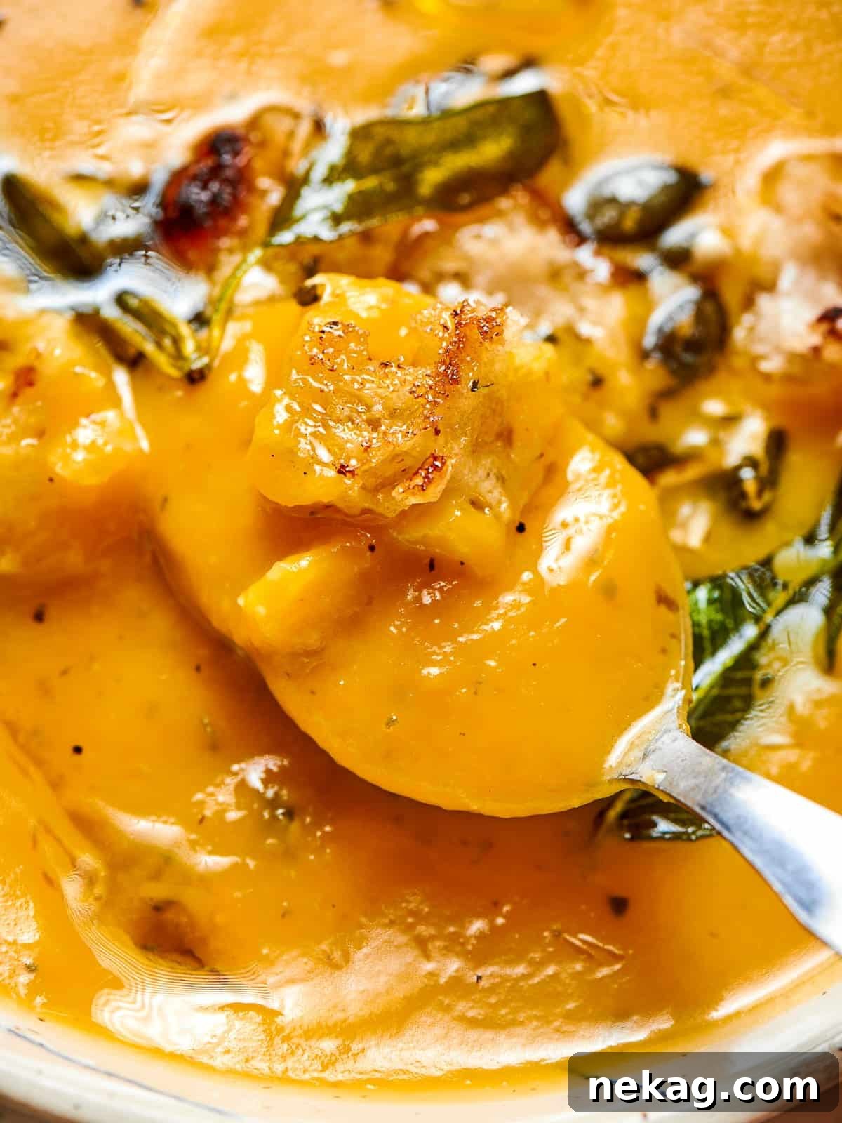 A large serving spoon gently dipping into a vibrant blue pot filled with creamy, golden squash soup, highlighting its thick, velvety texture and inviting warmth.