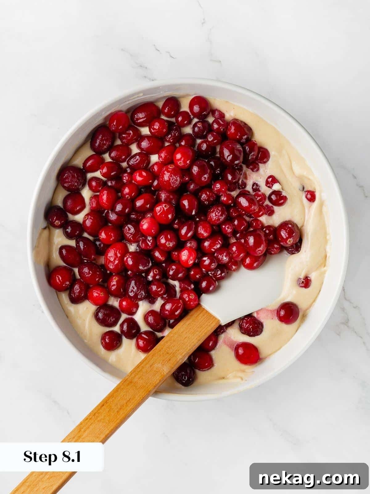 Jeweled Cranberry Cake 6 Fresh cranberries being gently folded into the light cake batter using a spatula, ensuring even distribution.