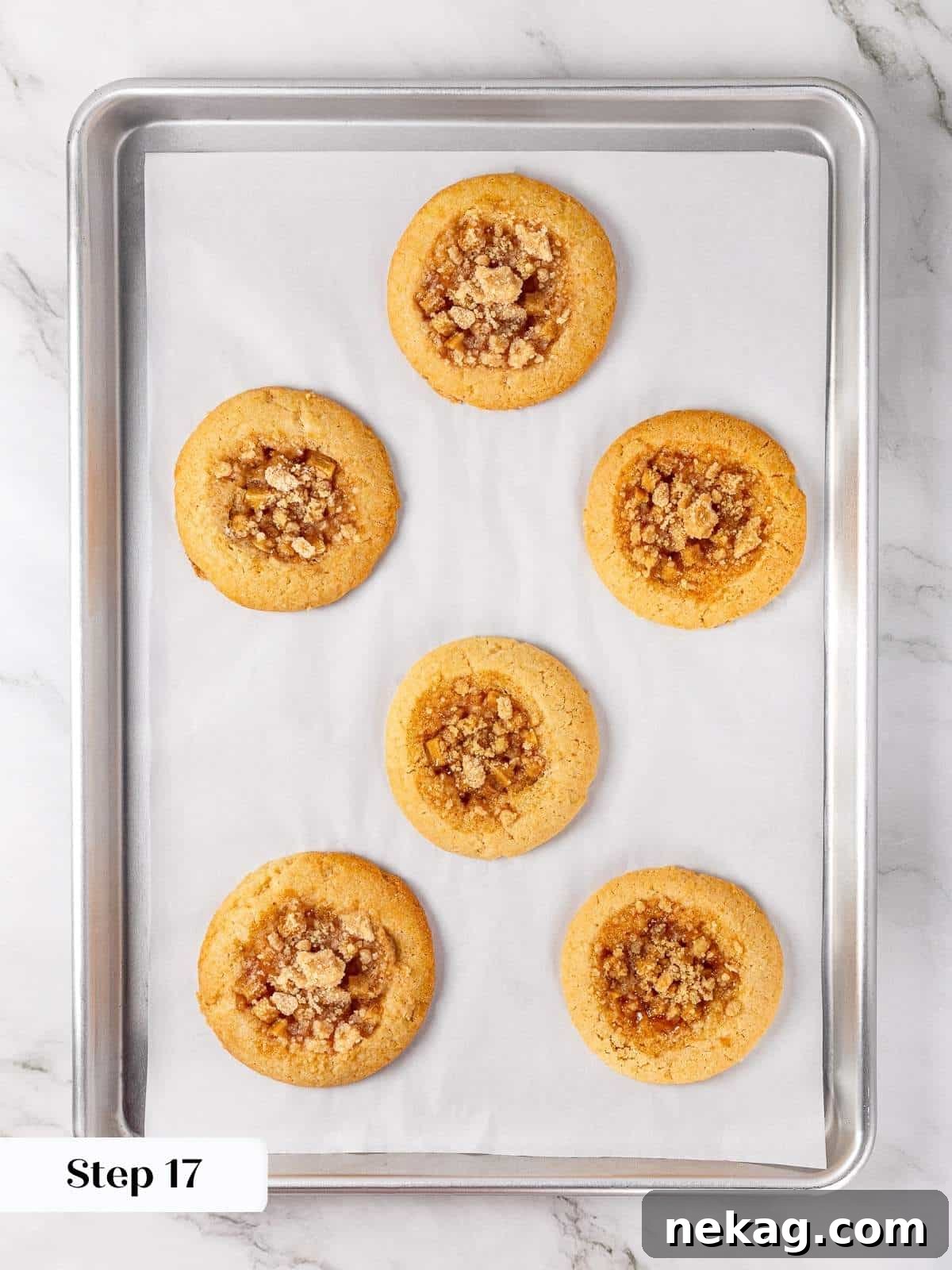 Apple Crumble Cookies 15 Freshly baked apple pie cookies cooling on a parchment-lined baking sheet after the oven.