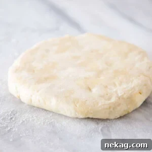 All-butter pie dough shaped into a disk on a marble surface, ready for chilling.