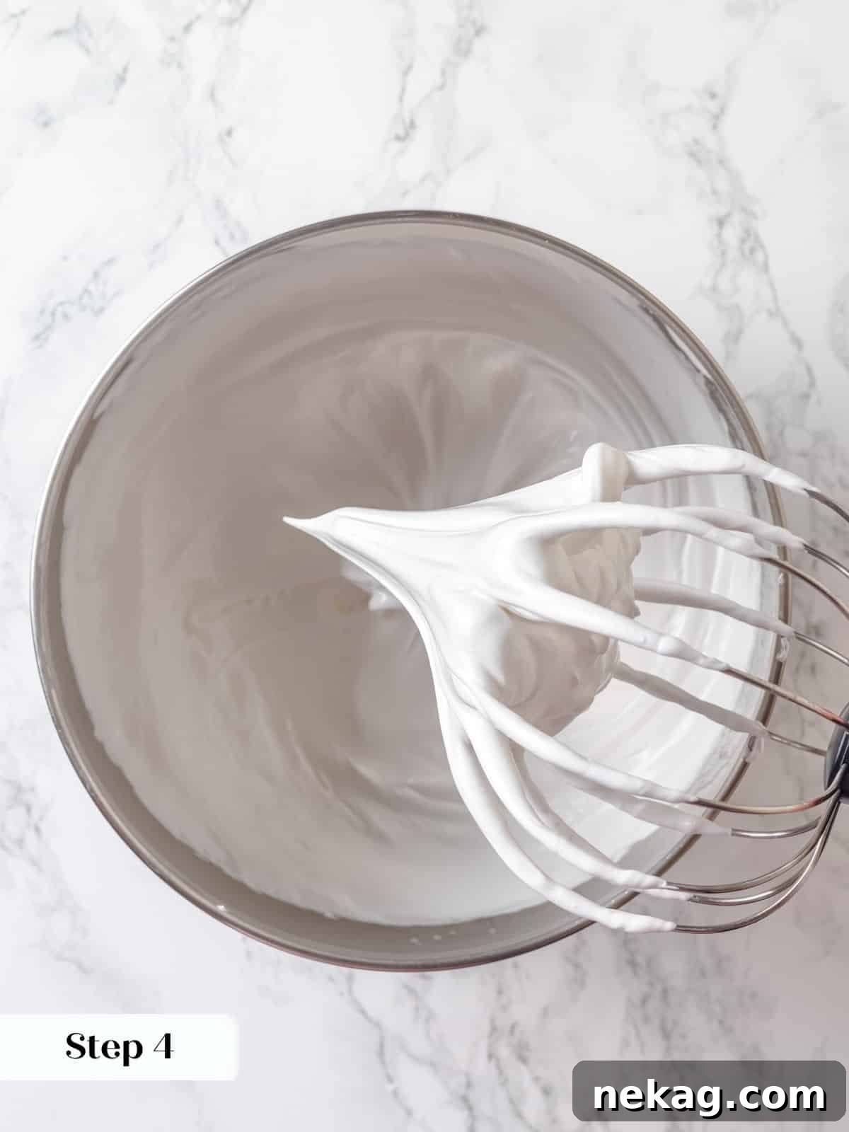 Whipped meringue reaching stiff peaks inside a stand mixer after heating egg whites, looking glossy and firm.