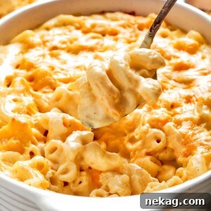 A large spoon lifting a creamy, cheesy scoop of baked mac and cheese from a casserole dish, highlighting its rich texture.
