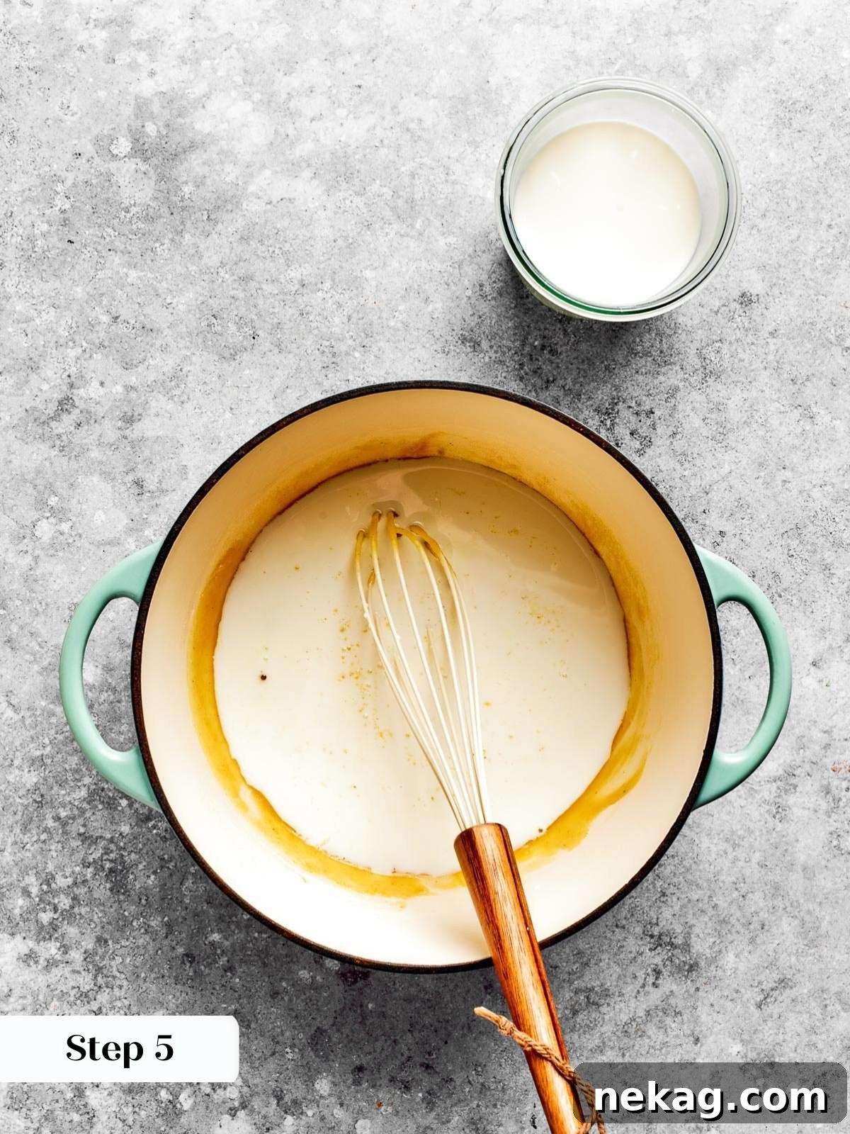 Ultimate Baked Mac and Cheese 9 Milk being gently poured into a thickened roux while whisking, creating a smooth and creamy base for the mac and cheese.