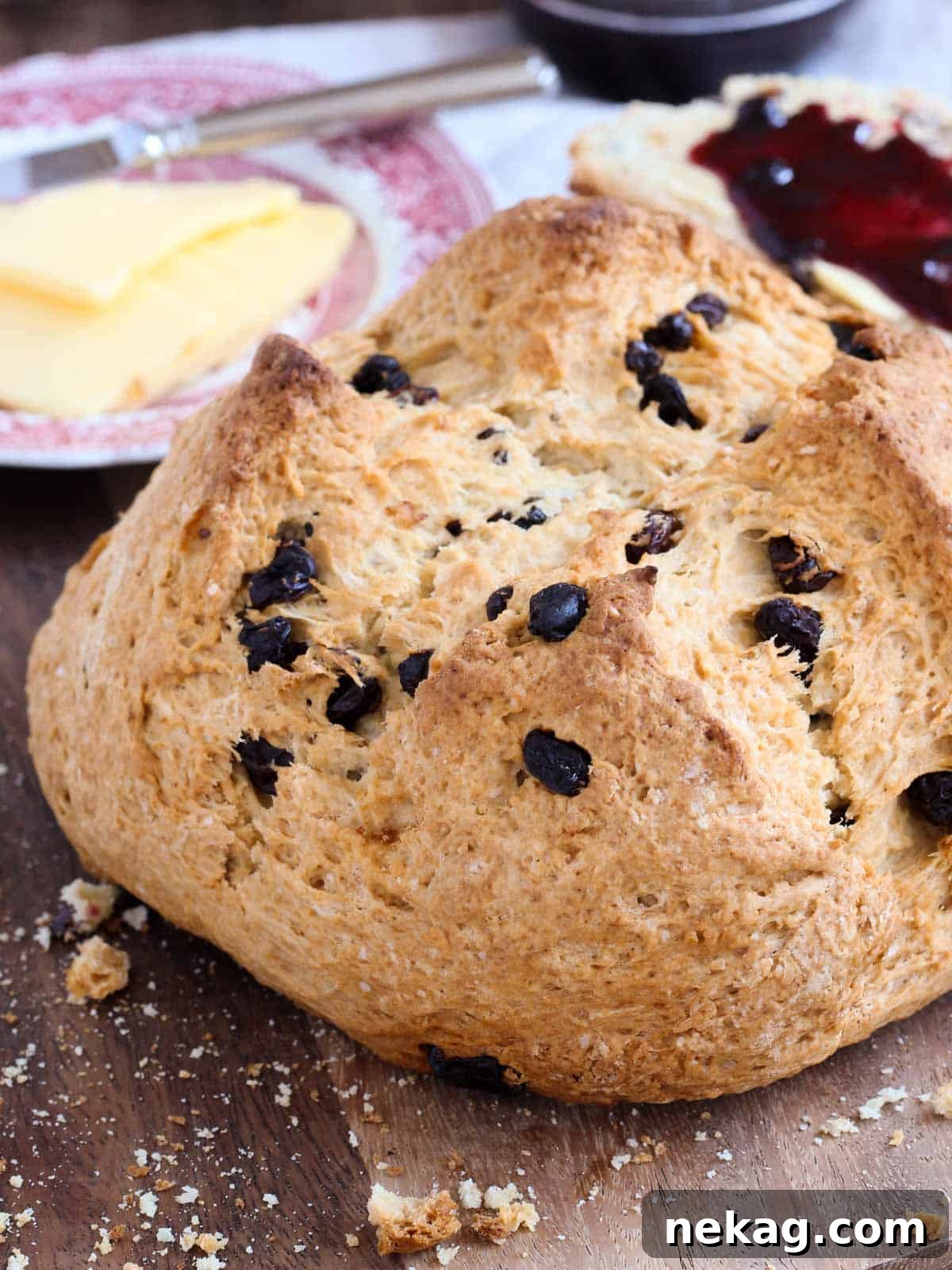Emerald Isle Raisin Loaf 2 A golden loaf of traditional Irish soda bread with raisins, perfectly sliced on a wooden board, surrounded by crumbs.