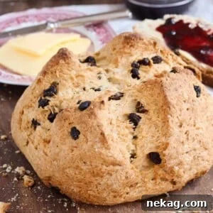 A beautifully baked round loaf of traditional Irish soda bread with raisins, with butter in the background.