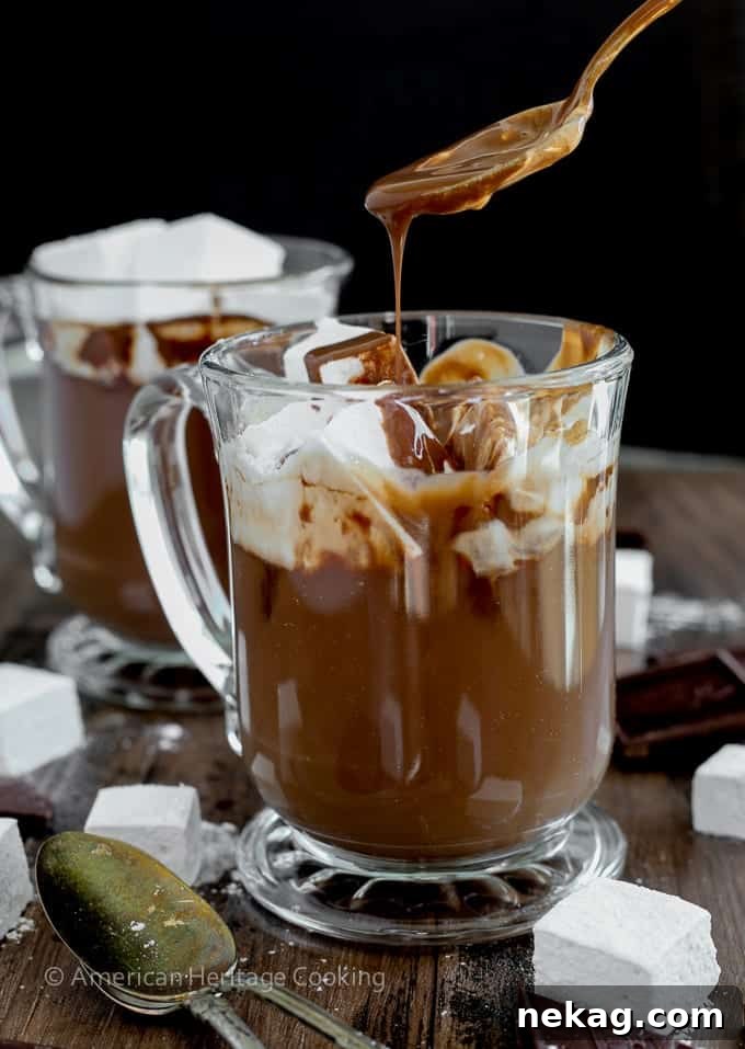 Two mugs of hot chocolate, one topped with marshmallows, on a rustic wooden surface.