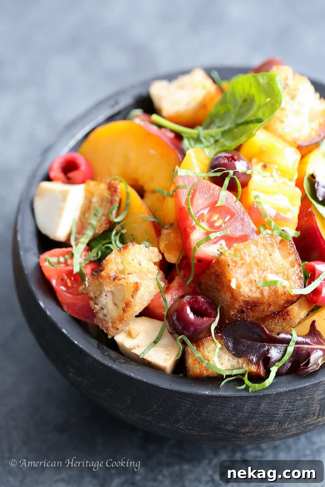 Orchard Caprese Panzanella 3 Close-up of a portion of Stone Fruit Caprese Panzanella Salad featuring fresh peaches, creamy mozzarella, and fragrant basil leaves.