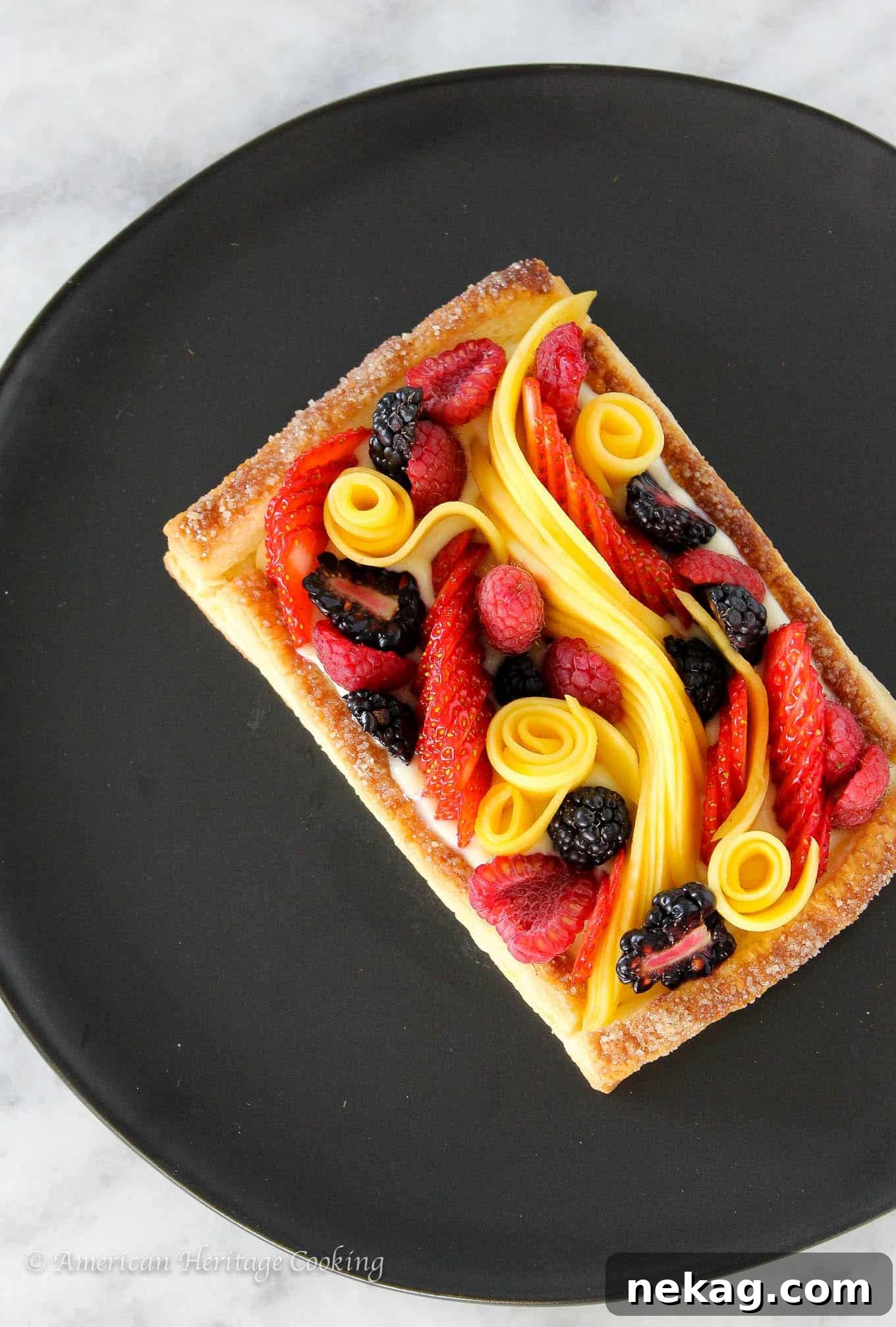 Vibrant Fruit Puff Pastry 2 Puff pastry fruit tart on a black plate set on a white marble surface, showcasing fresh berries and mango.