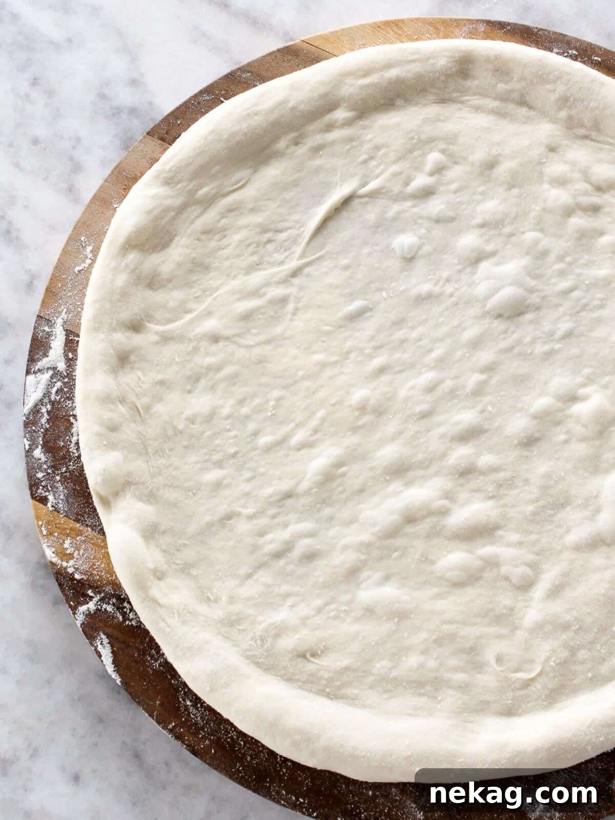 Ultimate Sourdough Pizza Dough Recipe 2 Unbaked pizza dough with raised edges and flour dusting, ready for toppings.