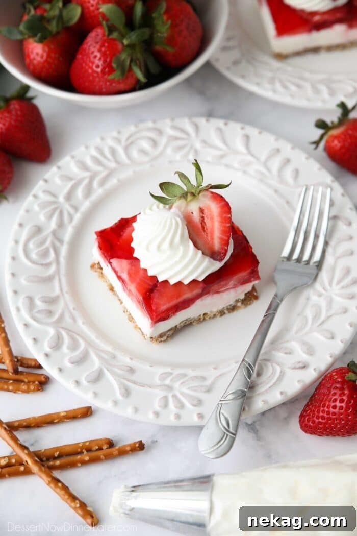 Piece of strawberry pretzel salad dessert on a plate garnished with whipped cream piped into a swirl with half of a strawberry.