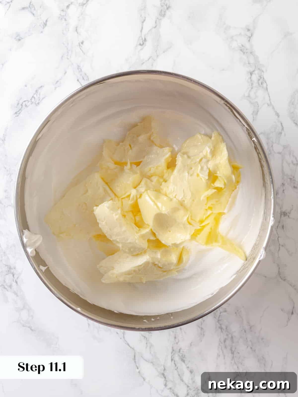 Sinfully Rich Chocolate Cake 18 Softened unsalted butter is being gradually added to the perfectly whipped meringue, an essential step for creating the smooth and luxurious frosting.