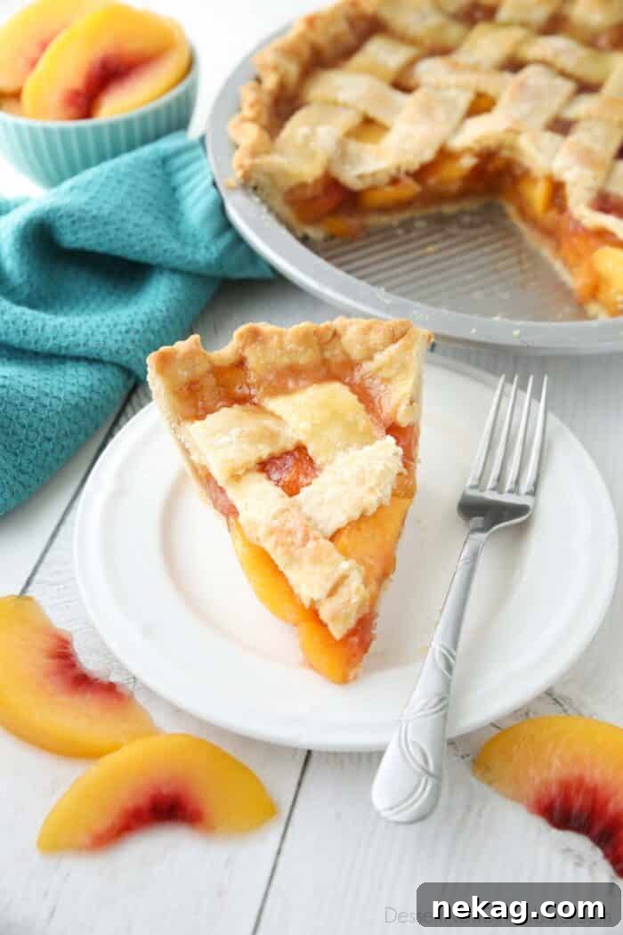 A perfectly baked slice of peach pie on a white plate, showcasing its golden crust and juicy peach filling.
