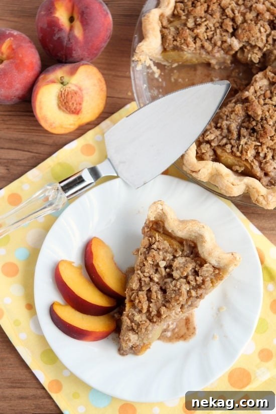 A tempting slice of peach pie topped with a golden-brown streusel crumb topping, served on a white plate.