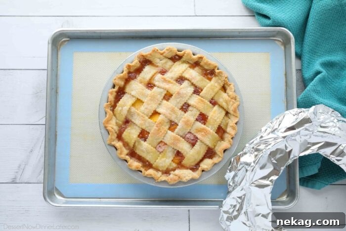 A golden-brown peach pie fresh out of the oven, with foil removed, revealing its perfectly baked crust.