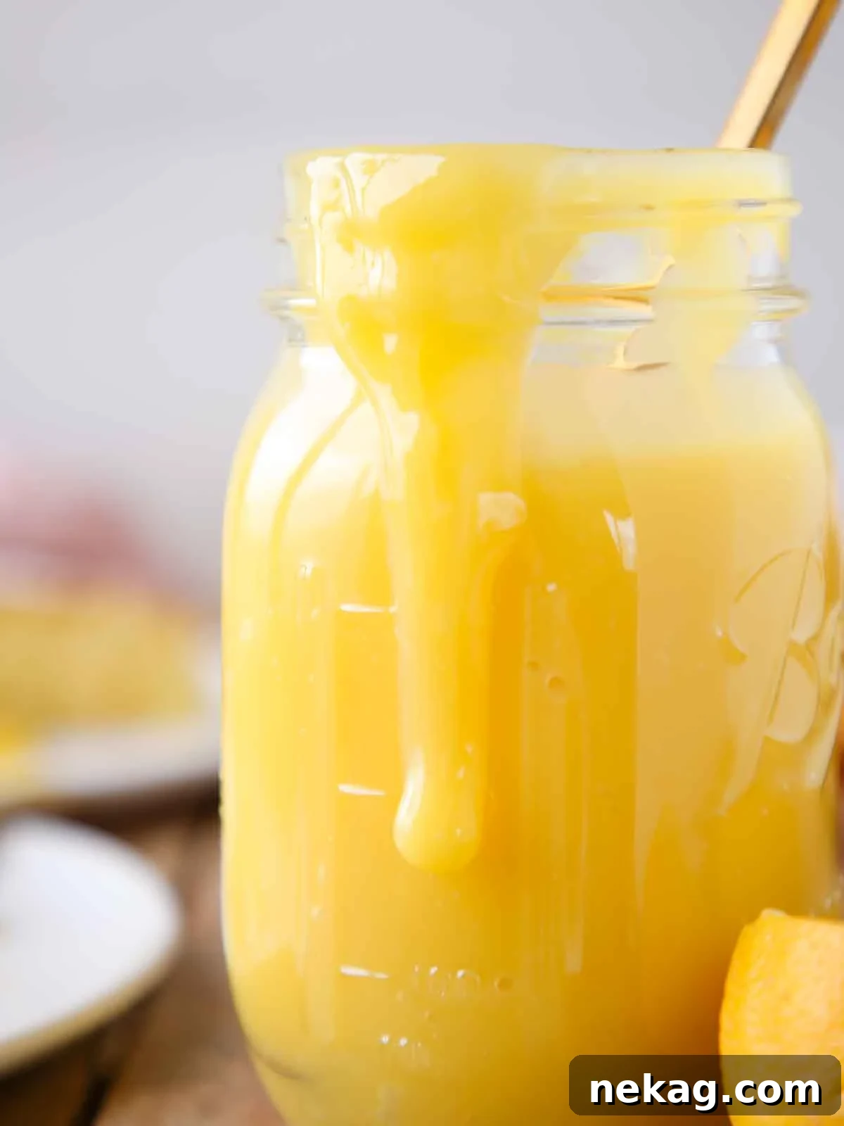 Smooth lemon curd in a mason jar with a slice of cake in the background, ready for serving.
