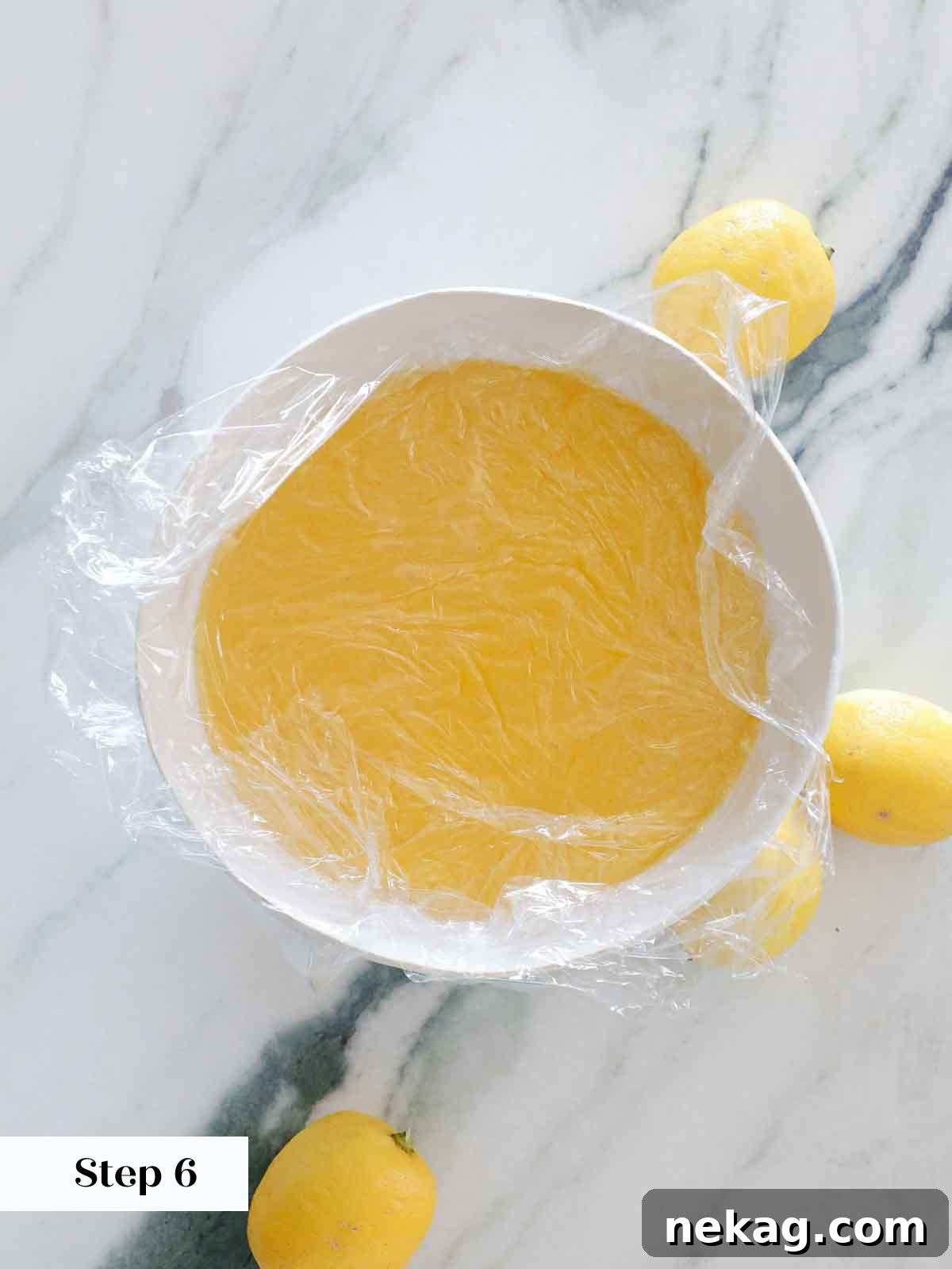 Hot lemon curd cooling in a white bowl, covered with plastic wrap directly on its surface to prevent skin formation.