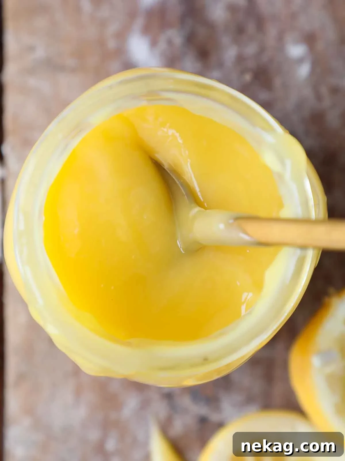 Close-up view of a jar of lemon curd with a spoon, highlighting its smooth, glossy texture.
