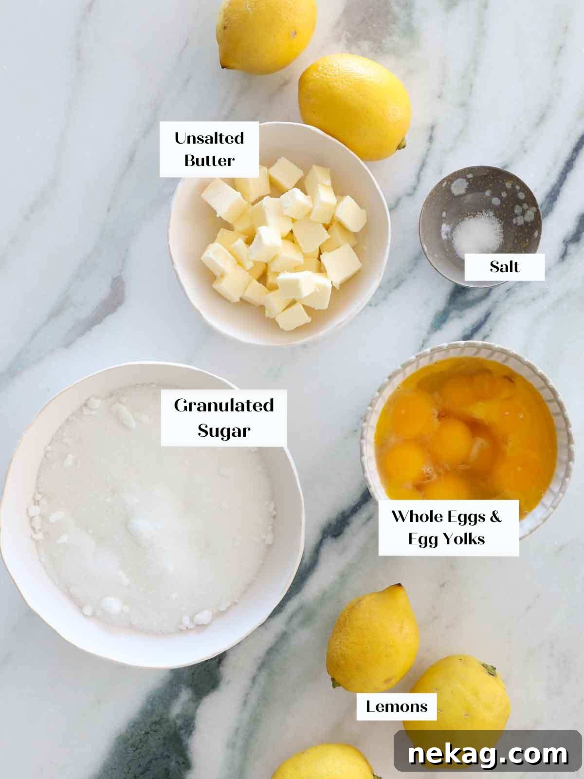 Fresh lemons, eggs, butter, and sugar laid out on a marble counter, representing the core ingredients for lemon curd.