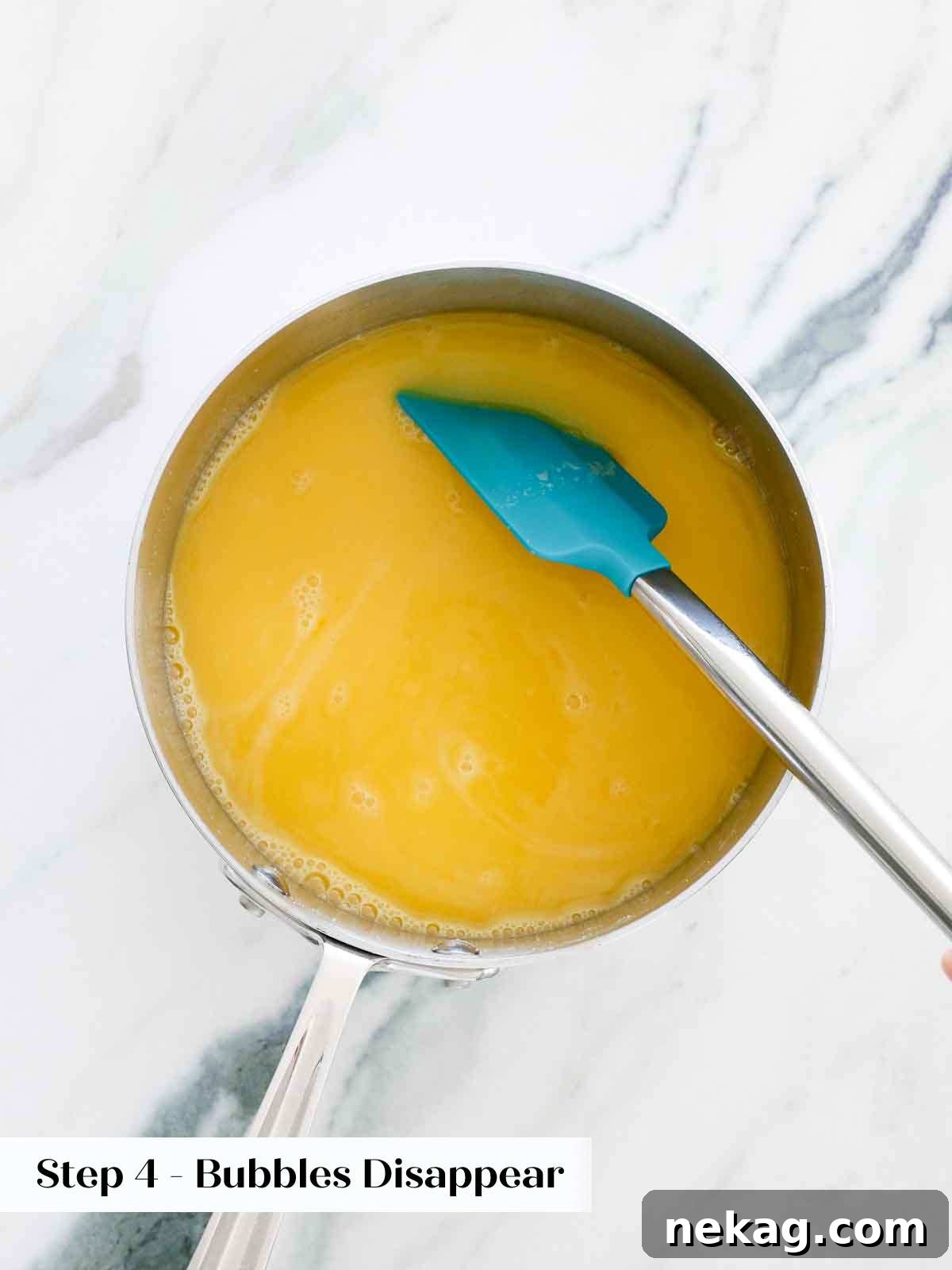 Lemon curd mixture being cooked in a saucepan over medium-low heat, with a spatula stirring.