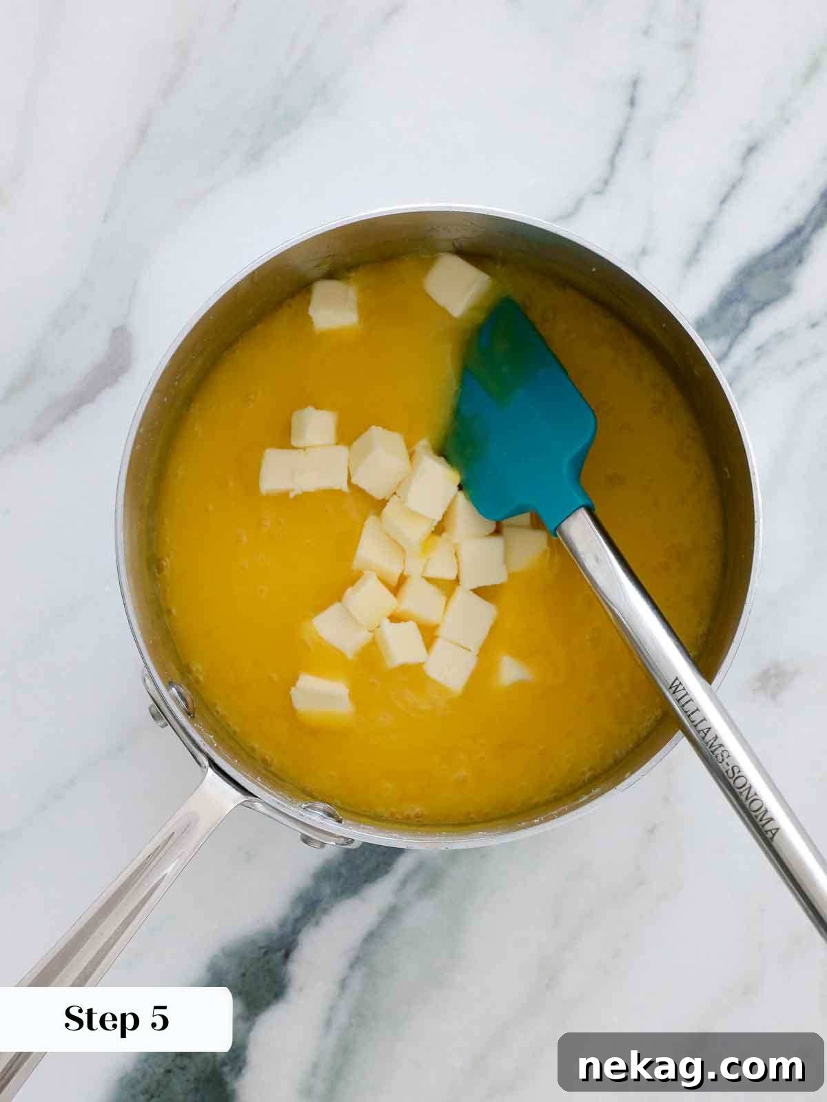 Cubed butter being added to hot lemon curd in a saucepan, ready to be stirred in.