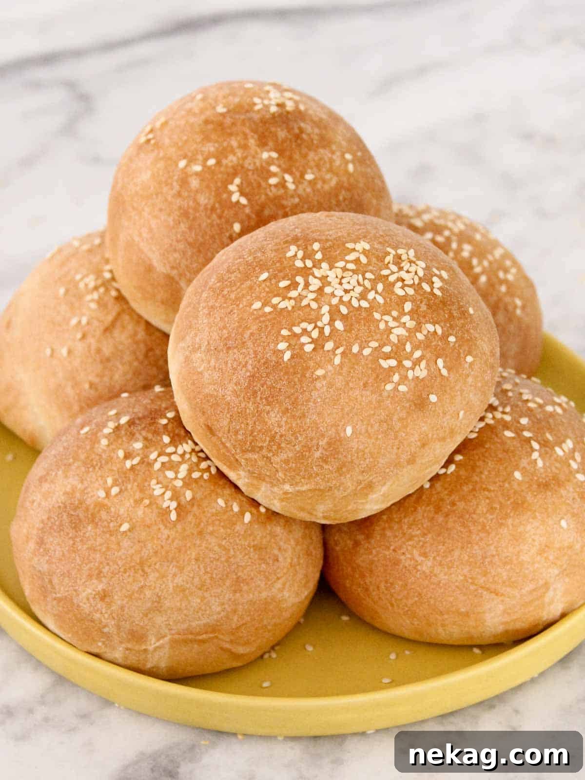 Pillowy Soft Brioche Buns 2 Homemade brioche hamburger buns with sesame seeds, perfectly golden, on a yellow plate.