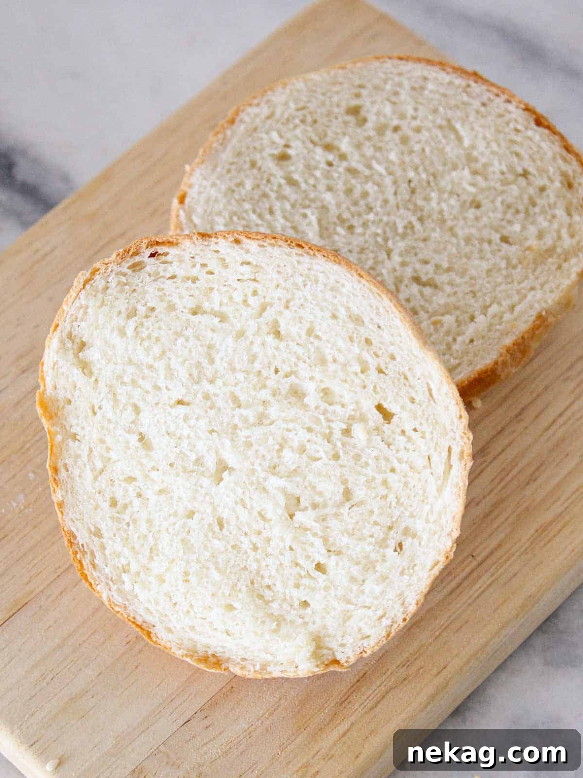Pillowy Soft Brioche Buns 3 A perfectly sliced brioche bun, revealing its soft and fluffy interior, rests on a wooden board.