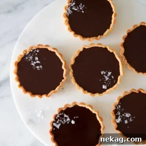 Decadent Chocolate Dreams 2 Close-up of a beautifully arranged plate of mini salted chocolate tarts on a marble stand, garnished with flaky sea salt.