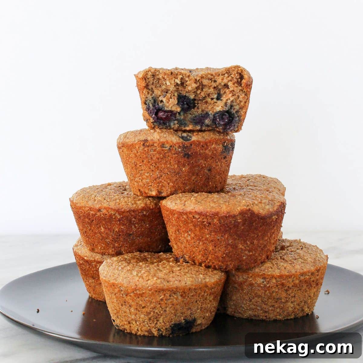 Protein-Powered Banana Muffins 3 A perfectly baked banana protein muffin with a bite taken, showcasing its soft, moist interior and even blueberry distribution, stacked with others for a tempting display.