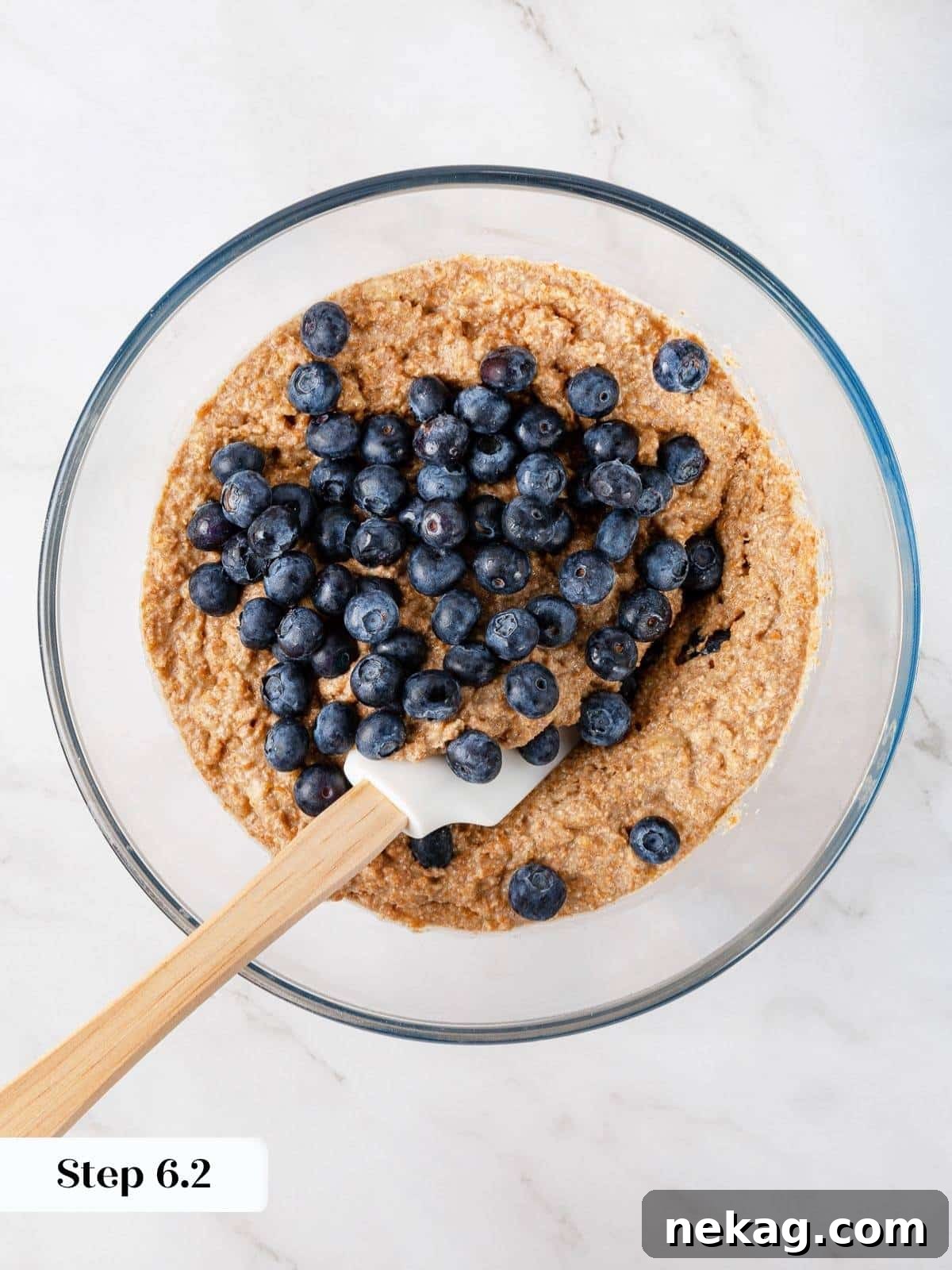 Protein-Powered Banana Muffins 9 Fresh or frozen blueberries being gently folded into the banana muffin batter with a spatula, ensuring even distribution of fruit without overmixing the delicate batter.