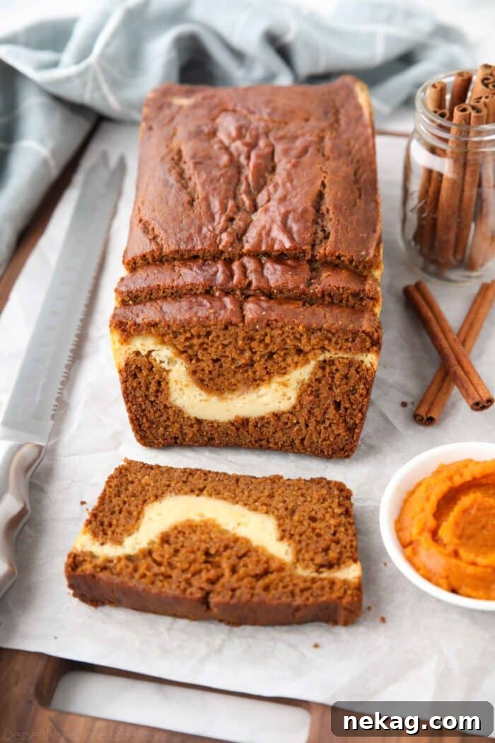 Swirled Pumpkin Cream Cheese Bread 2 A loaf of pumpkin cream cheese bread with a few slices cut, showing a swirl of cream cheese in the center.