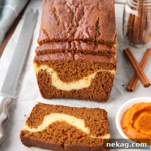 A loaf of pumpkin cream cheese bread with a few slices cut, showing a swirl of cream cheese in the center.