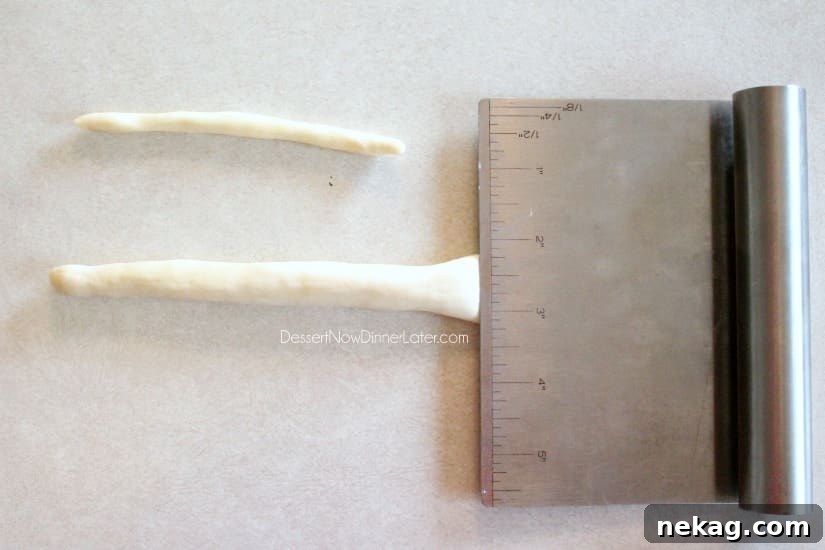 One end of a dough rope is flattened with a bench scrape, preparing it for bristles.