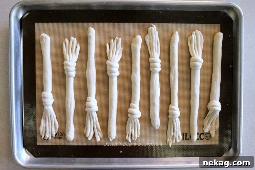 A child's hands helping to shape Witch's Broomstick Breadsticks on a baking sheet, showing the fun and ease of the activity.