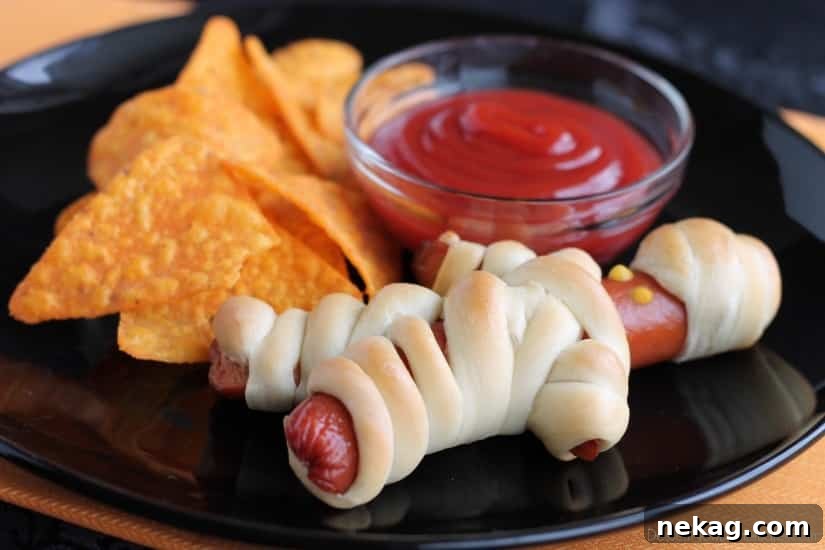 Two freshly baked Hot Dog Mummies with mustard eyes on a white plate, ready for a Halloween celebration.