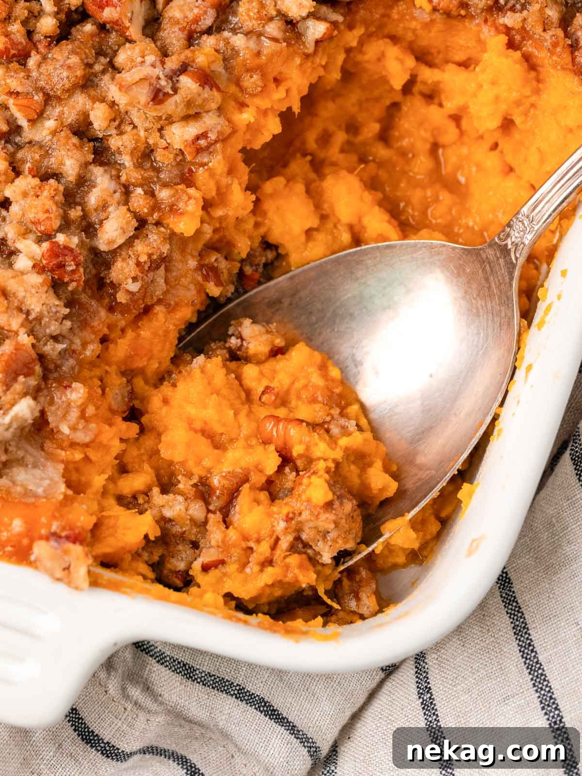 Golden-brown sweet potato casserole in a pristine white baking dish, ready for serving with a large spoon.