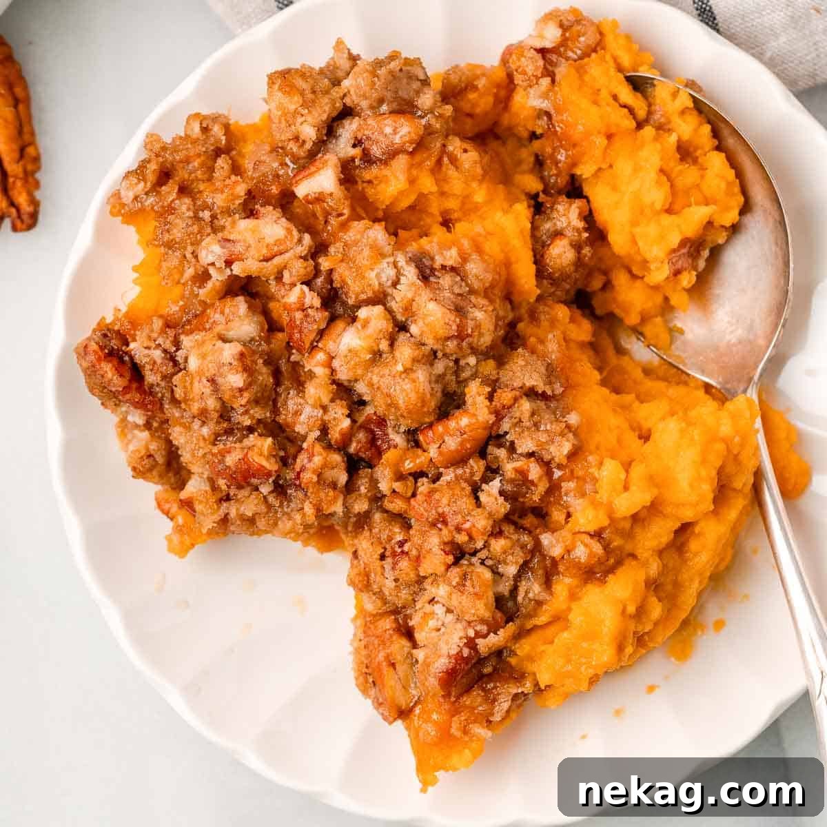 A serving of maple sweet potato casserole with pecan topping on a white plate, ready to be enjoyed.