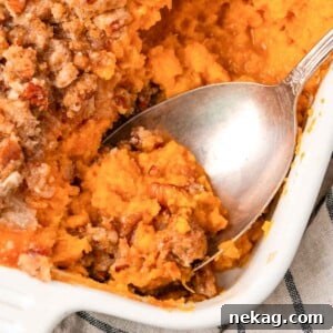A scoop of sweet potato casserole being served onto a plate, showcasing its rich texture and crunchy topping.