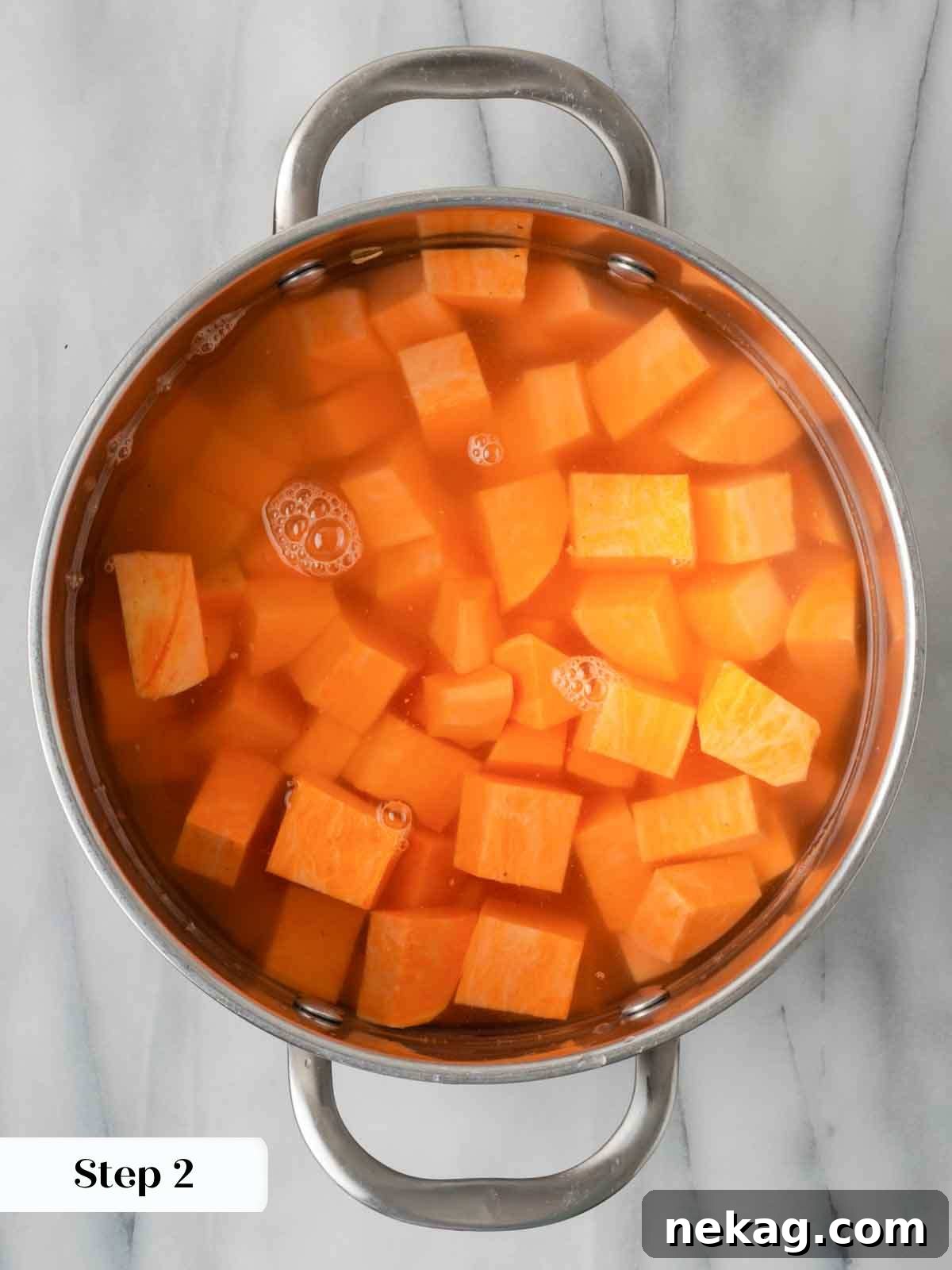 Cubed sweet potatoes simmering in a pot of cold water on a stovetop.