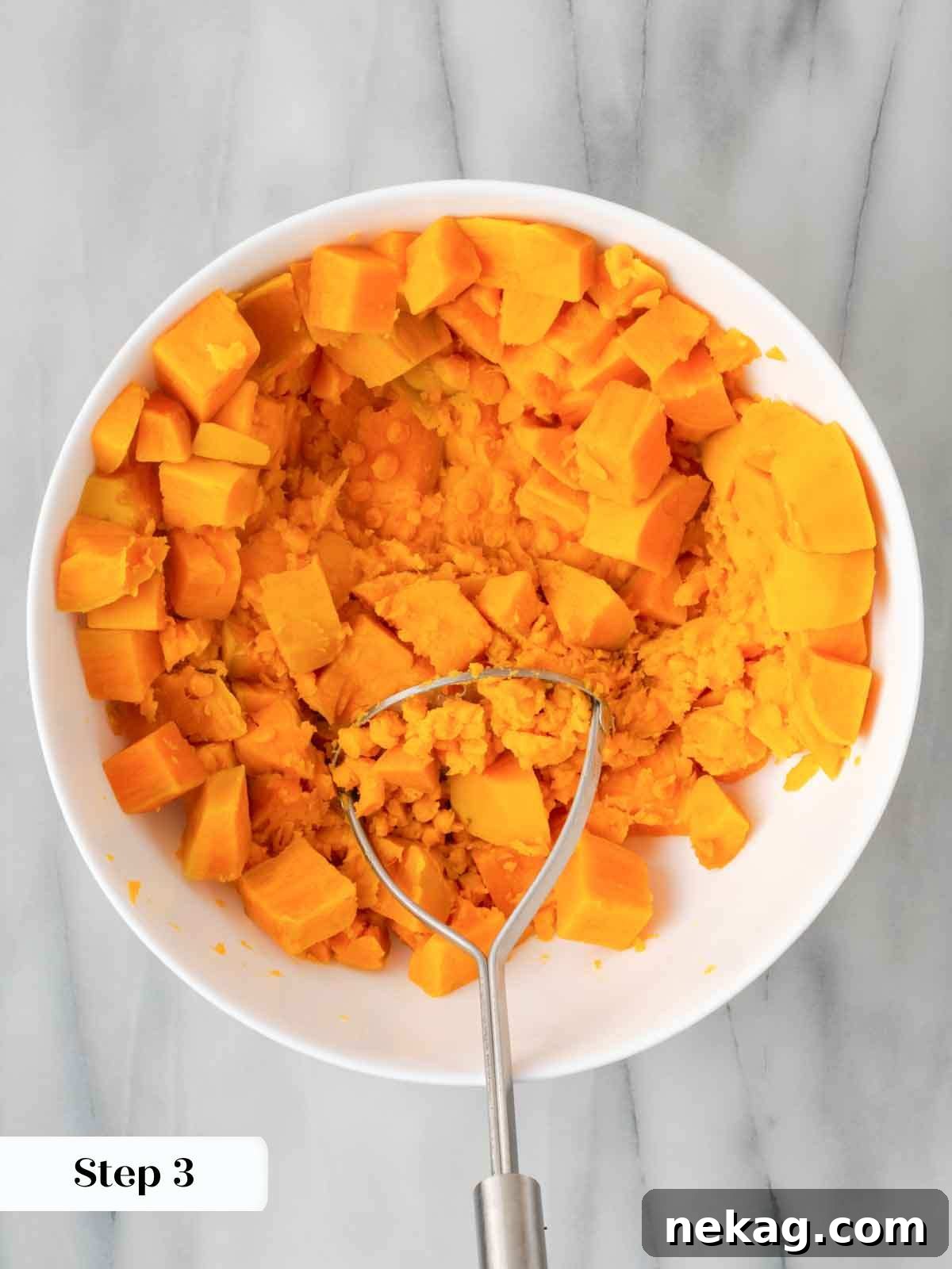 Mashed sweet potatoes being prepared in a large mixing bowl, creating a smooth puree.