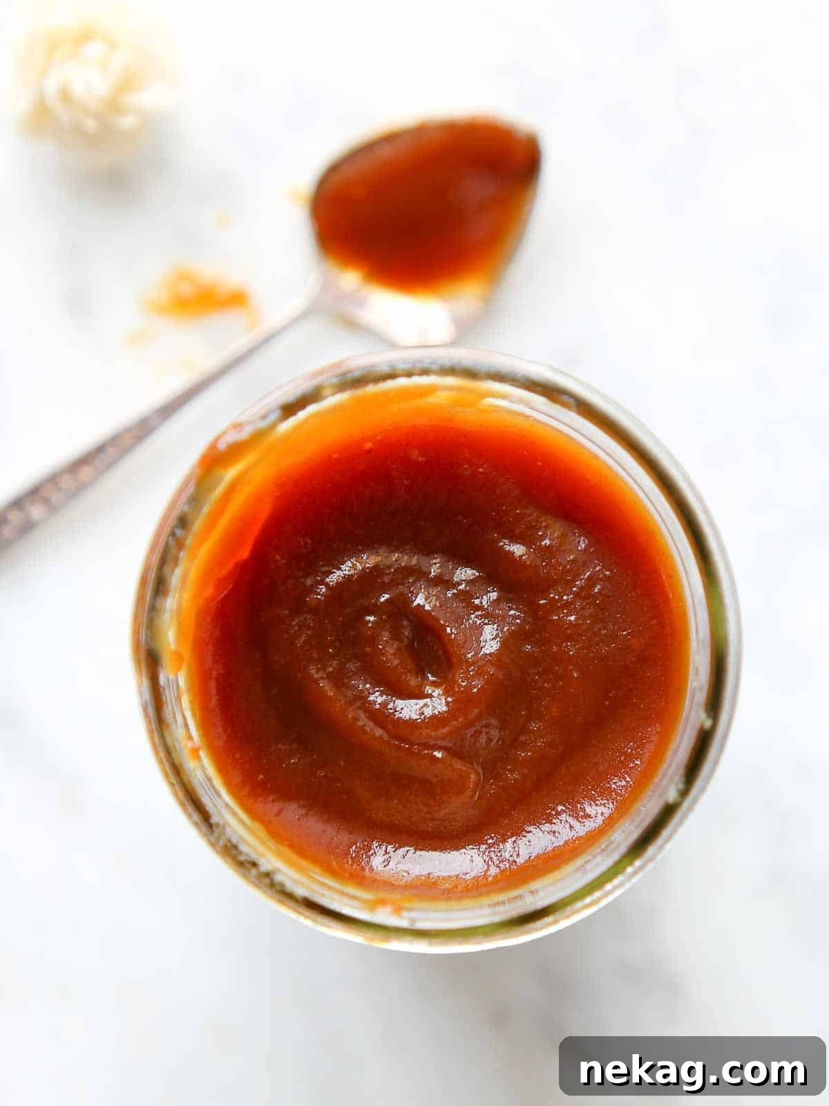 Homemade apple butter in a clear mason jar on a marble surface, ready to be enjoyed or stored.